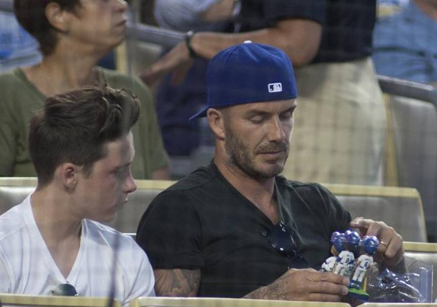 Sotto lo sguardo incuriosito del figlio, barba incolta e cappellino d’ordinanza: “Becks” osserva i bobbleheads dei Dodgers. (Lapresse)